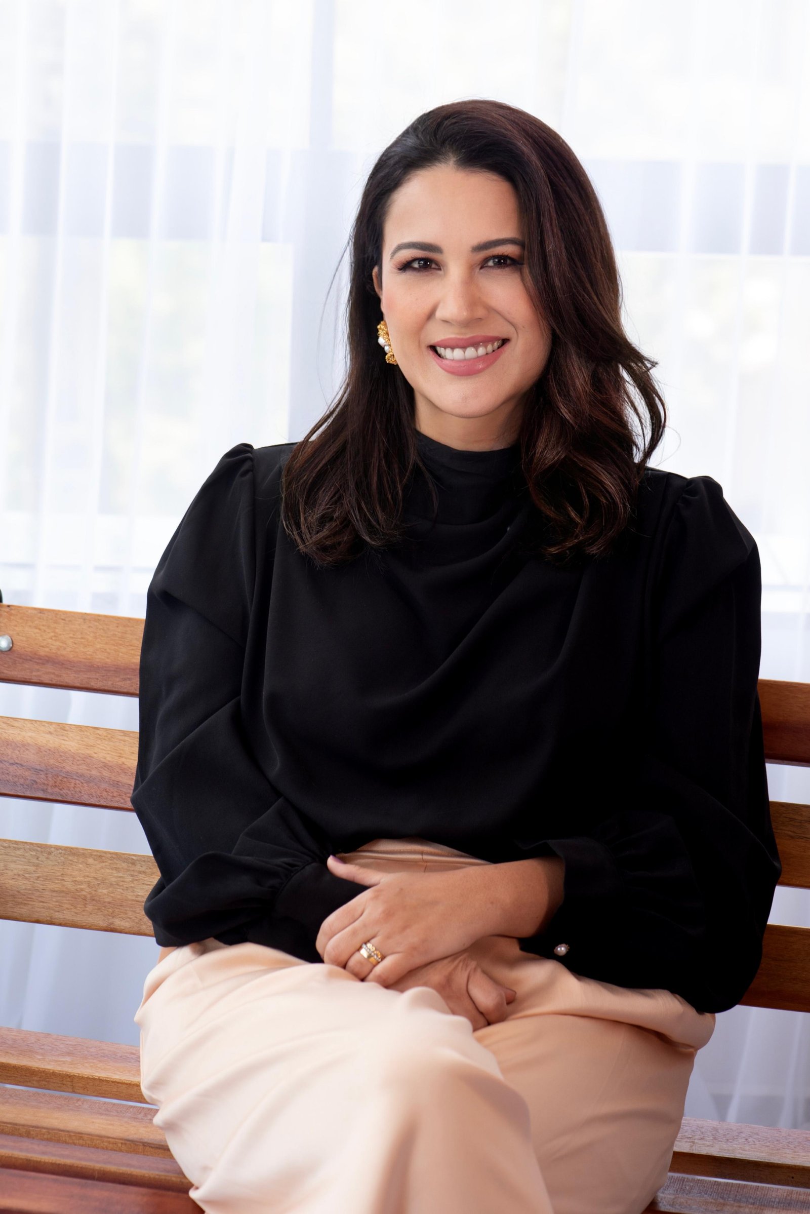 Dra. Ludimila Seko sorrindo, sentada em banco de madeira